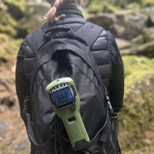 Vandrare med svart ryggsäck i skogslandskap, Thermacell MR300 fäst på ryggsäcken.