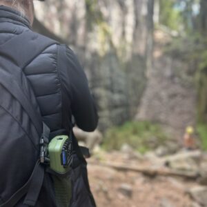 Person på vandring med ryggsäck och bärbar fläkt i skogsmiljö.