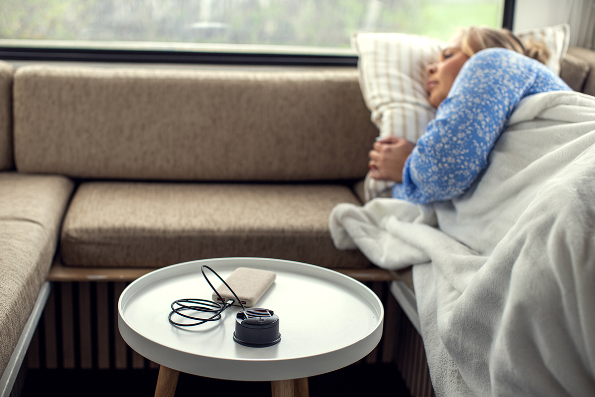 Sovande kvinna på soffa med kuddar, en bordslampa och laddare i fokus.
