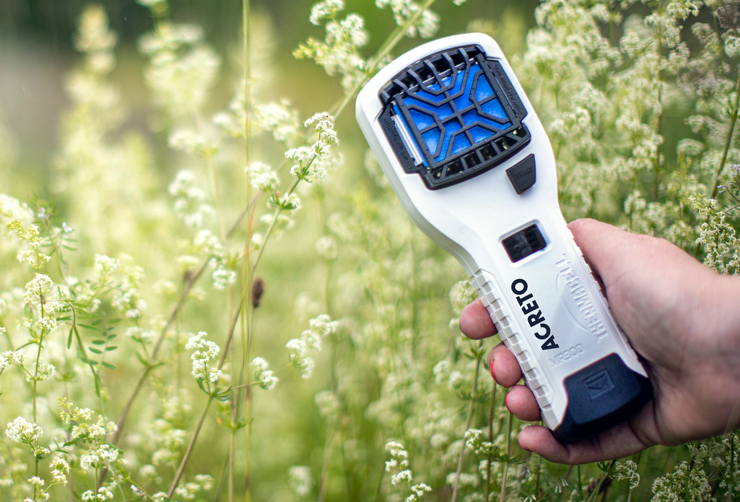 Hand håller en Agreto-enhet bland vilda blommor i naturen.