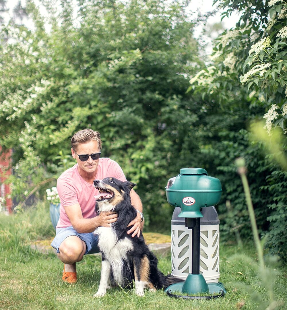 En man, en hund som står jämte en Mosquito Magnet enhet på sommaren