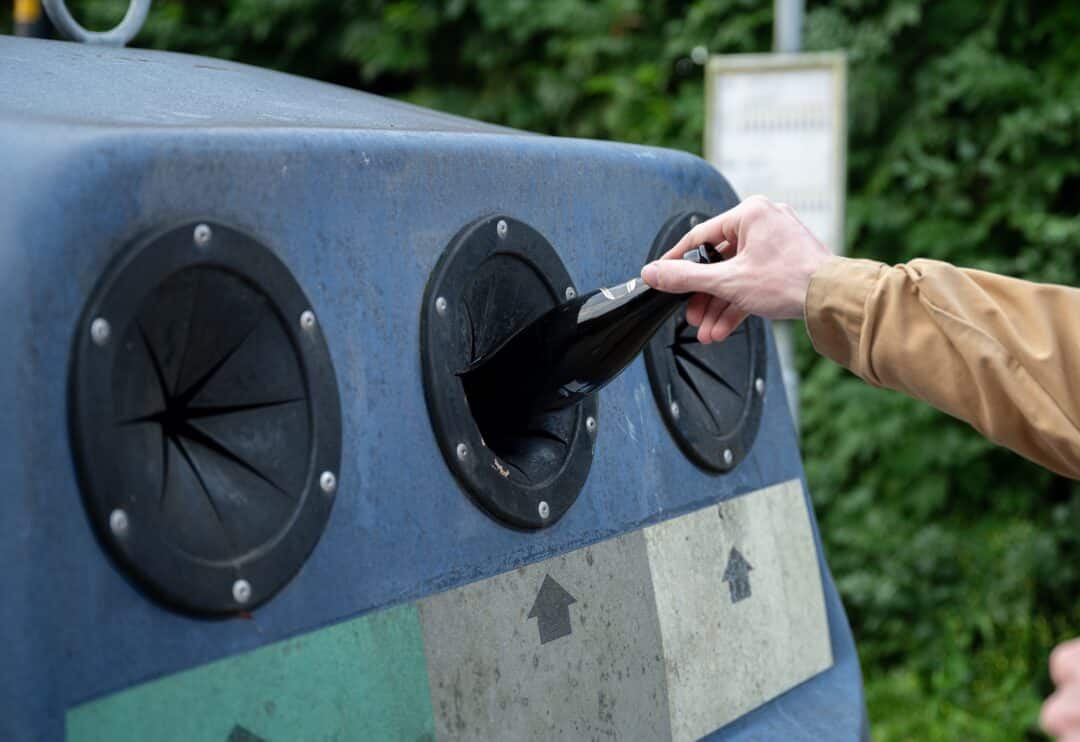 Sortera glasflaskor: person återvinner vid behållare.