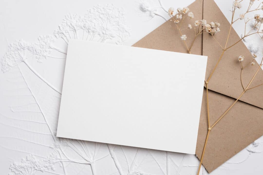 Vit pappersark på kuvert med torkade blommor, minimalistisk design.