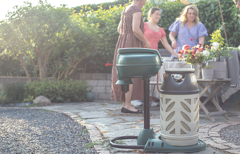 Grön grill och gasflaska i en solig trädgård med människor som umgås.