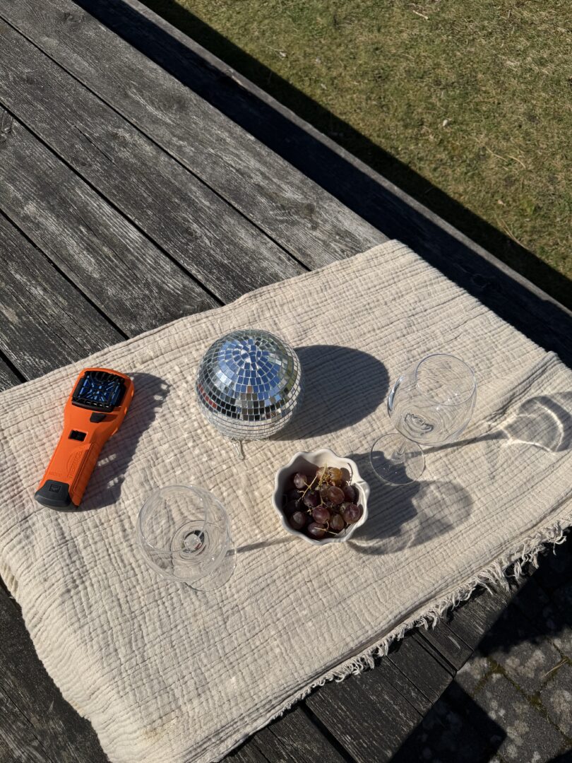 En solig utomhusmatsituation med en spegelboll, glas och vindruvor på ett bord.
